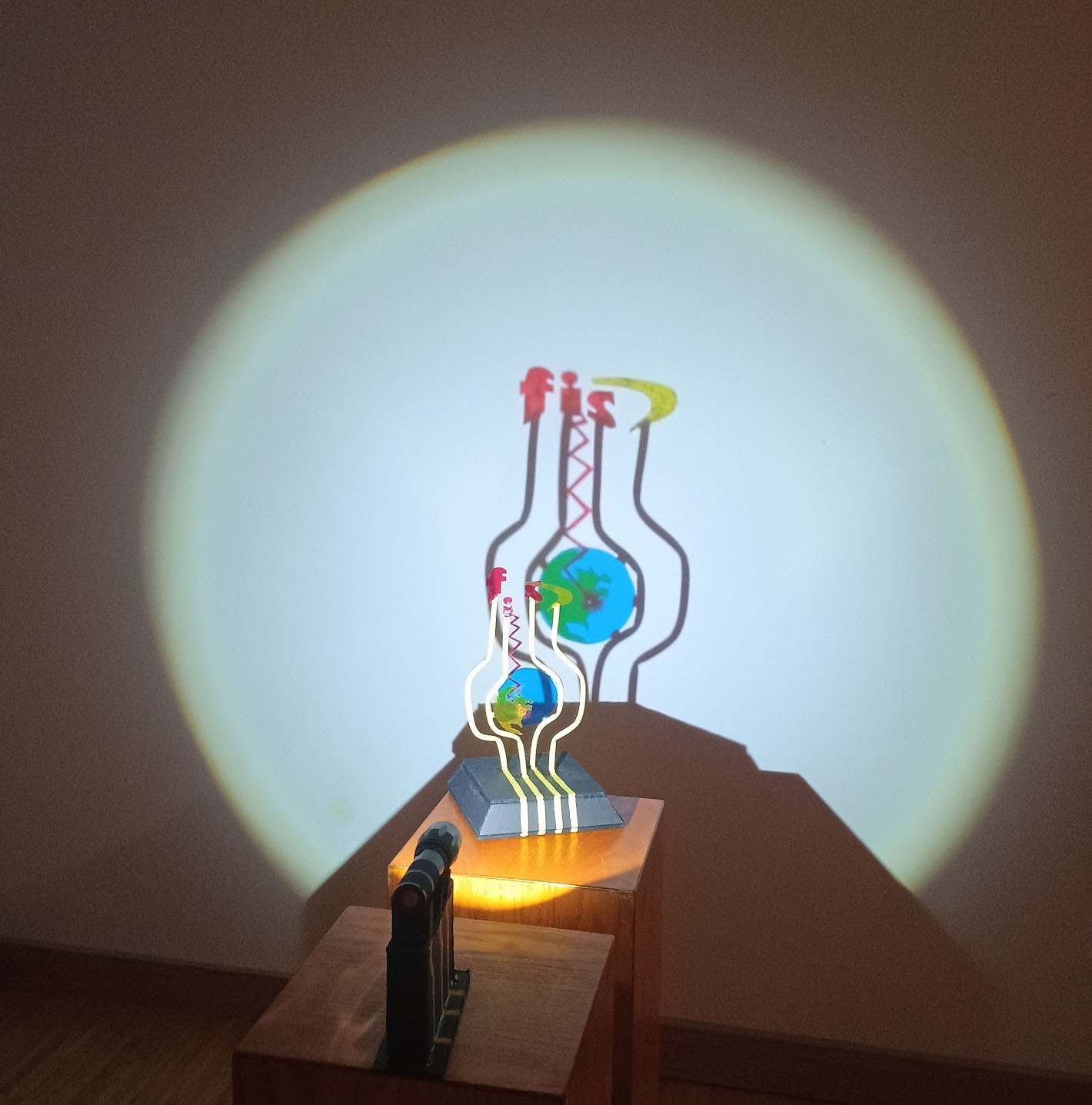 photo of a sculpture whose parts assemble visually with light to project a globe and FIS logo onto the wall